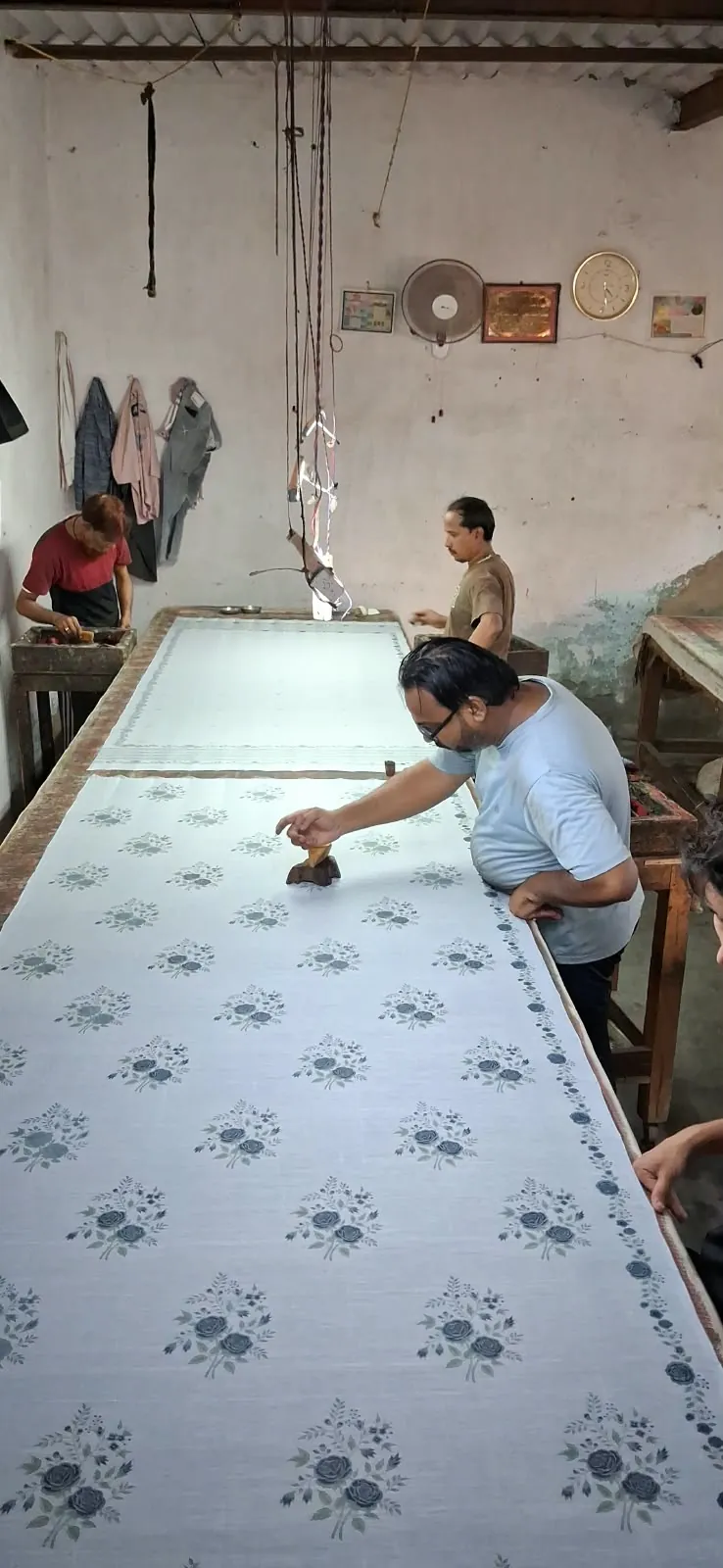 Fabloom block printer stamping a floral buti in indigo onto white fabric on a long printing table in Noida