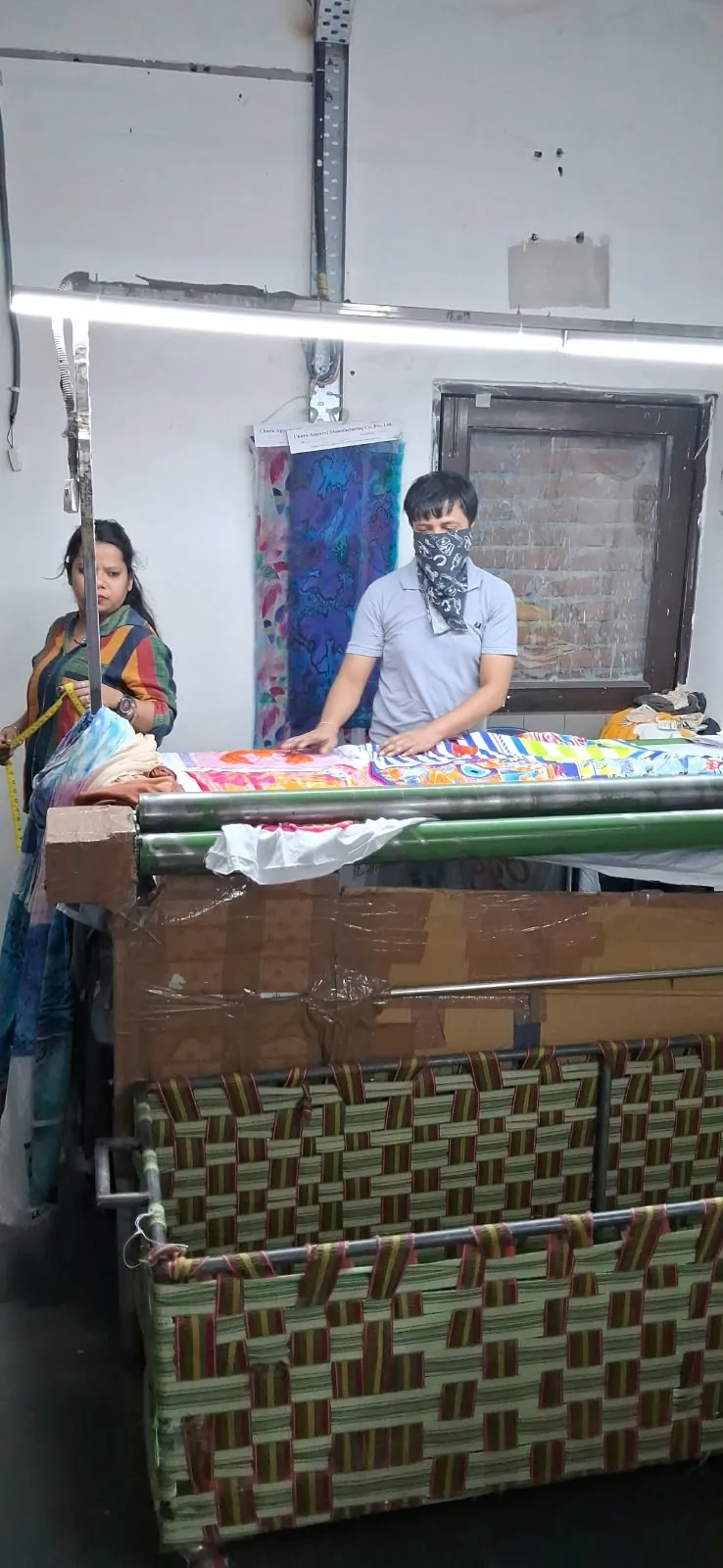 Team checking a length of brightly printed fabric as it comes off the roller