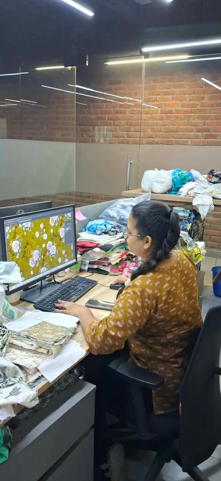Designer recolouring a floral print on a mustard ground, with fabric swatches on the desk