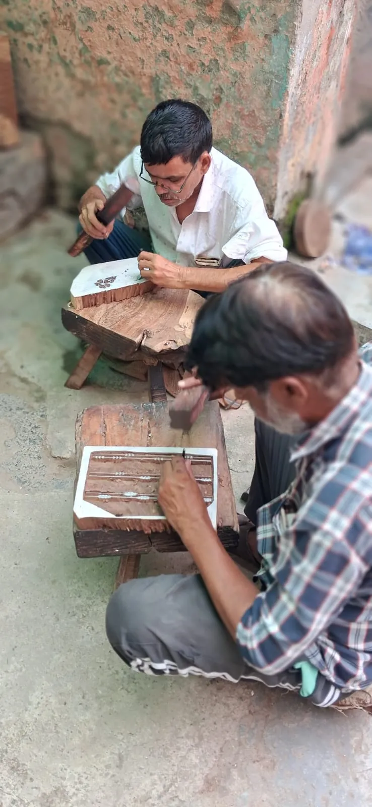 Two Fabloom artisans hand carving custom wooden print blocks with chisel and mallet in Bhagalpur